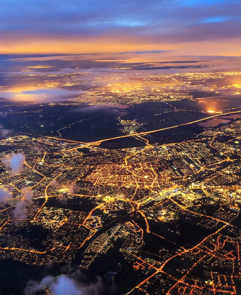 Aerial night view of a city's illuminated power grid and street network, representing smart grid automation.